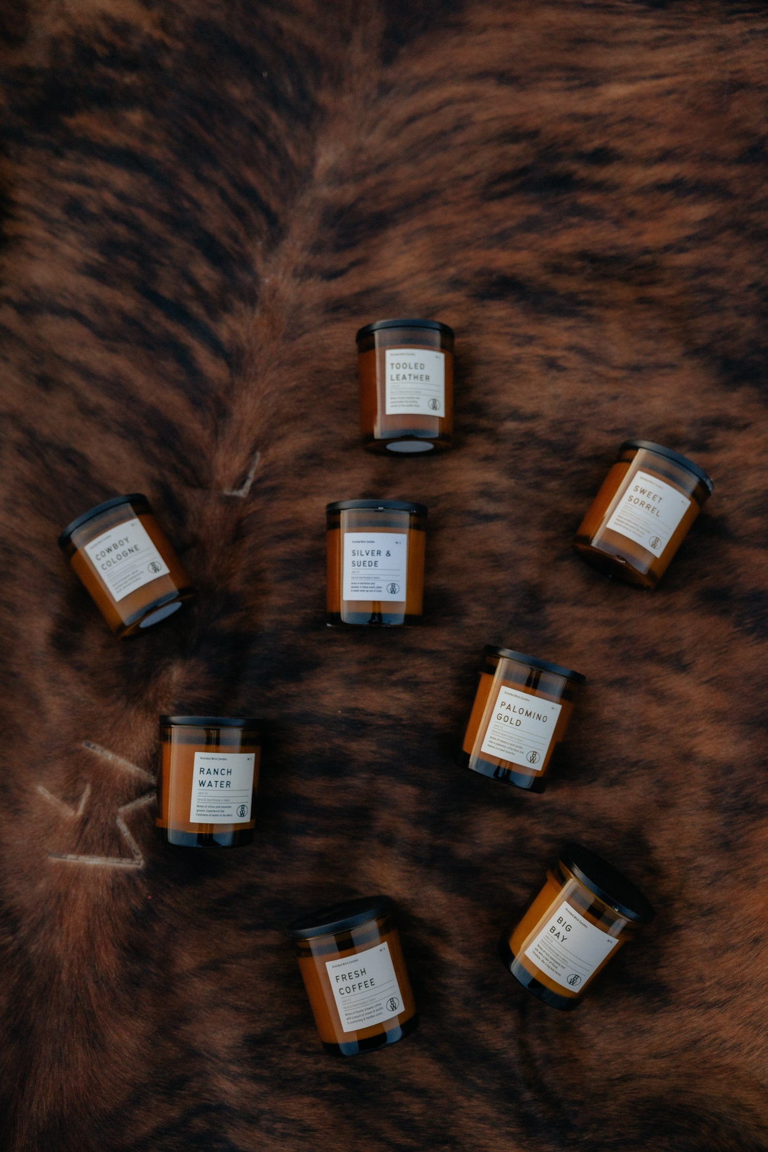 The image shows a candle jar labeled "Cowboy Cologne" in an amber glass container. 